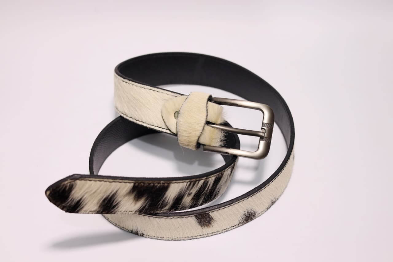 Black and white cowhide belt with a silver buckle on a light gray background